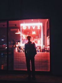 Rear view of man standing in illuminated building at night