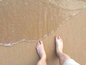 Low section of man standing on shore at beach