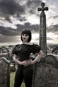 Portrait of goth woman standing in cemetery against sky