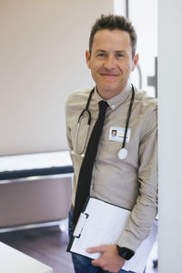 Portrait of smiling doctor leaning on wall at hospital