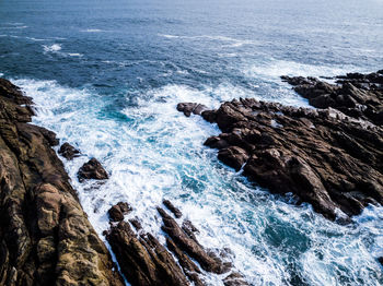 High angle view of waves splashing on rock formations at beach