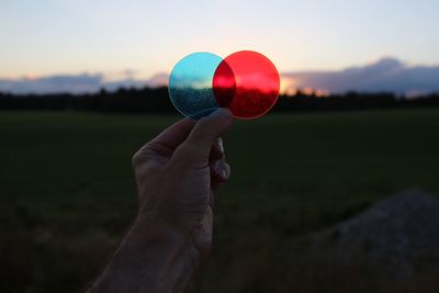 Cropped hand of man holding plastic circles against sky