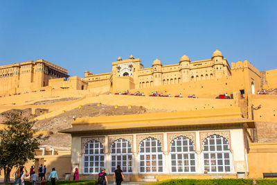 Group of people in front of historical building against clear blue sky