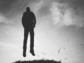 Silhouette man levitating above grass against sky