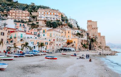 People on beach by buildings against sky in city