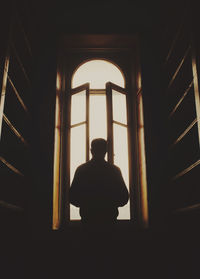 Rear view of silhouette man looking through window in building