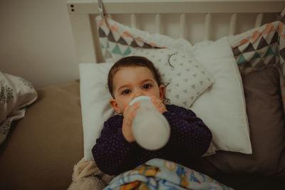 High angle portrait of cute boy girl drinking milk while lying on bed