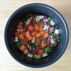 High angle view of chopped vegetables and oxtail in slow cooker bowl on table