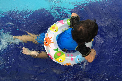 Rear view of boy floating with inflatable ring in swimming pool