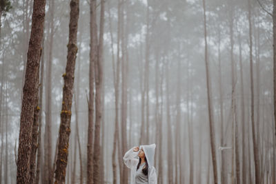 Woman wearing raincoat while standing against trees in forest