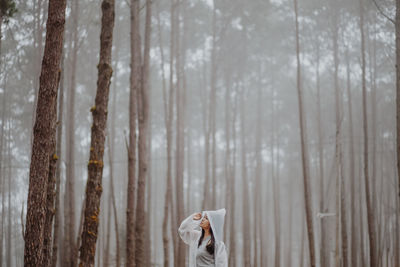 Man standing by tree trunk in forest