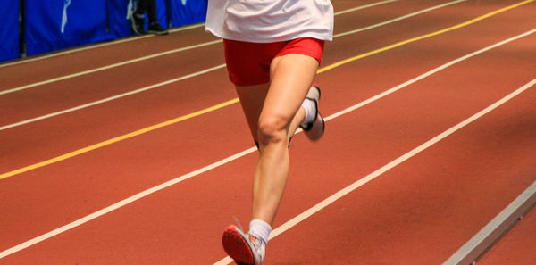 Front view of the legs of a track and field runner racing on an indoor track.