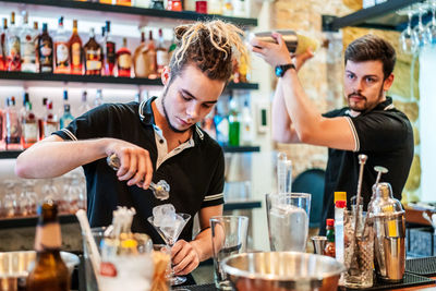 Barmen in uniform preparing alcohol beverages together while shaking cocktails and putting ice cubes in glasses