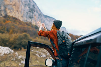 Rear view of woman standing on car against mountain