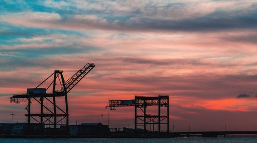 Silhouette cranes against sky during sunset