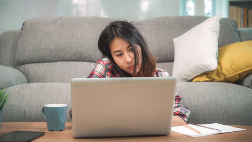 Young woman using mobile phone while sitting on sofa at home