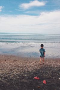 Rear view of boy standing on beach against sky