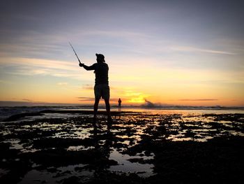 Silhouette fisherman standing against sea during sunset