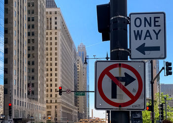 Road sign by buildings against blue sky