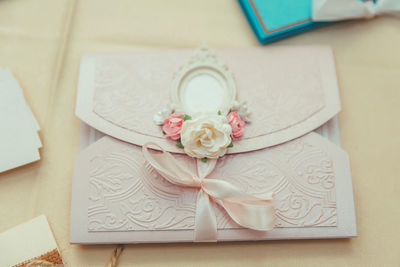 An envelope with soft pink embossing, decorated with a light pink ribbon, artificial roses