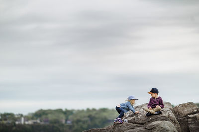 Young girl trying to climb to meet her older brother on a rock summer