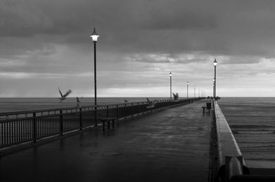 Street lights on pier by sea against sky