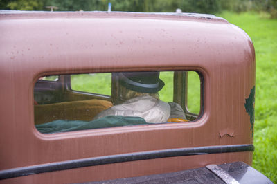 An elderly woman in hat and raincoat is driving in old antique vintage retro car in brown colours
