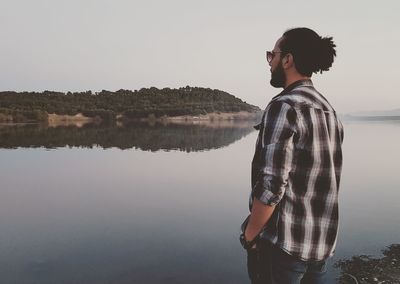 Side view of young man looking at lake against sky