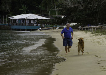 Full length of man running with dog on shore at beach