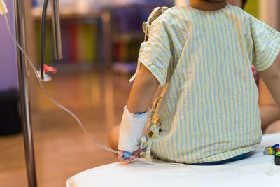 Midsection of boy sitting on bed in hospital