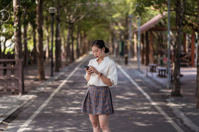 Ethnic asian female using smartphone and walking along tanya shen green bikeway in taichung