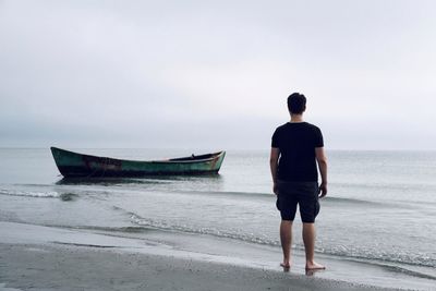 Rear view of mid adult man standing at beach against cloudy sky