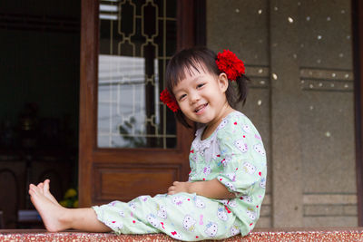 Cute girl wearing red flowers while sitting on retaining wall