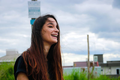 Portrait of smiling young woman in city against sky