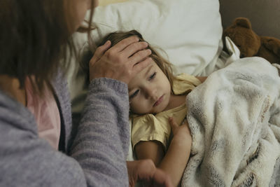 Portrait of sad engrossed sick little girl and her mother touching daughter's forehead