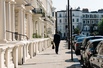 Rear view of man walking on street amidst buildings in city