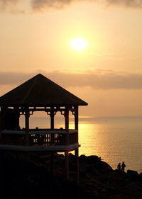 Gazebo on cliff against sea at sunset