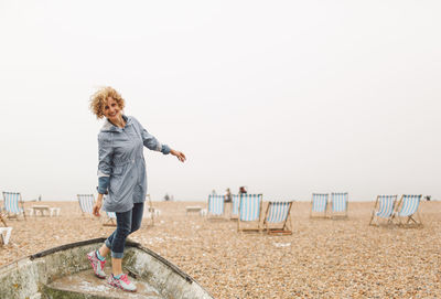 Cheerful woman standing on boat at beach against clear sky