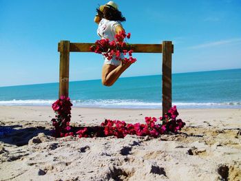 Woman sitting on beach by sea against sky