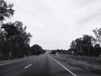 Empty road along trees and against sky