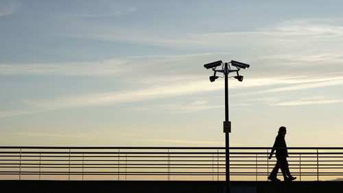 Silhouette man standing by railing and cctv against sky