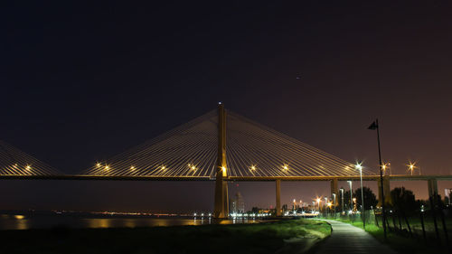 Illuminated bridge over river against sky at night