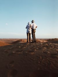 Rear view of men standing on desert against sky