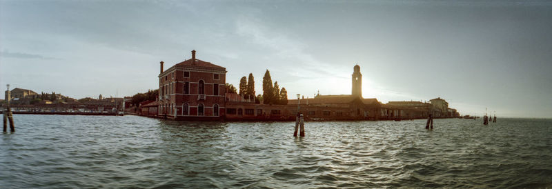 View of buildings by sea against cloudy sky