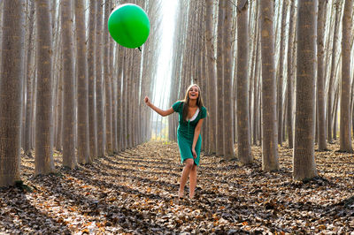 Full length of young woman holding balloon at forest