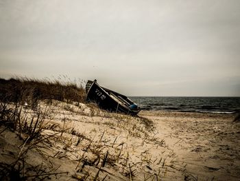 Abandoned boat at beach against sky