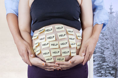 Midsection of pregnant woman with text on belly standing at home