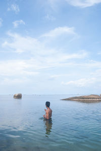 Shirtless man standing in water at beach against sky