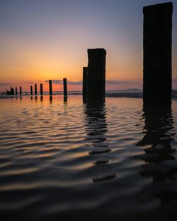 Silhouette of wooden posts in sea at sunset