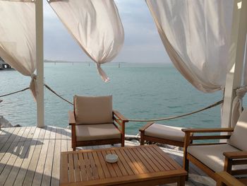 Chairs and table by sea against sky